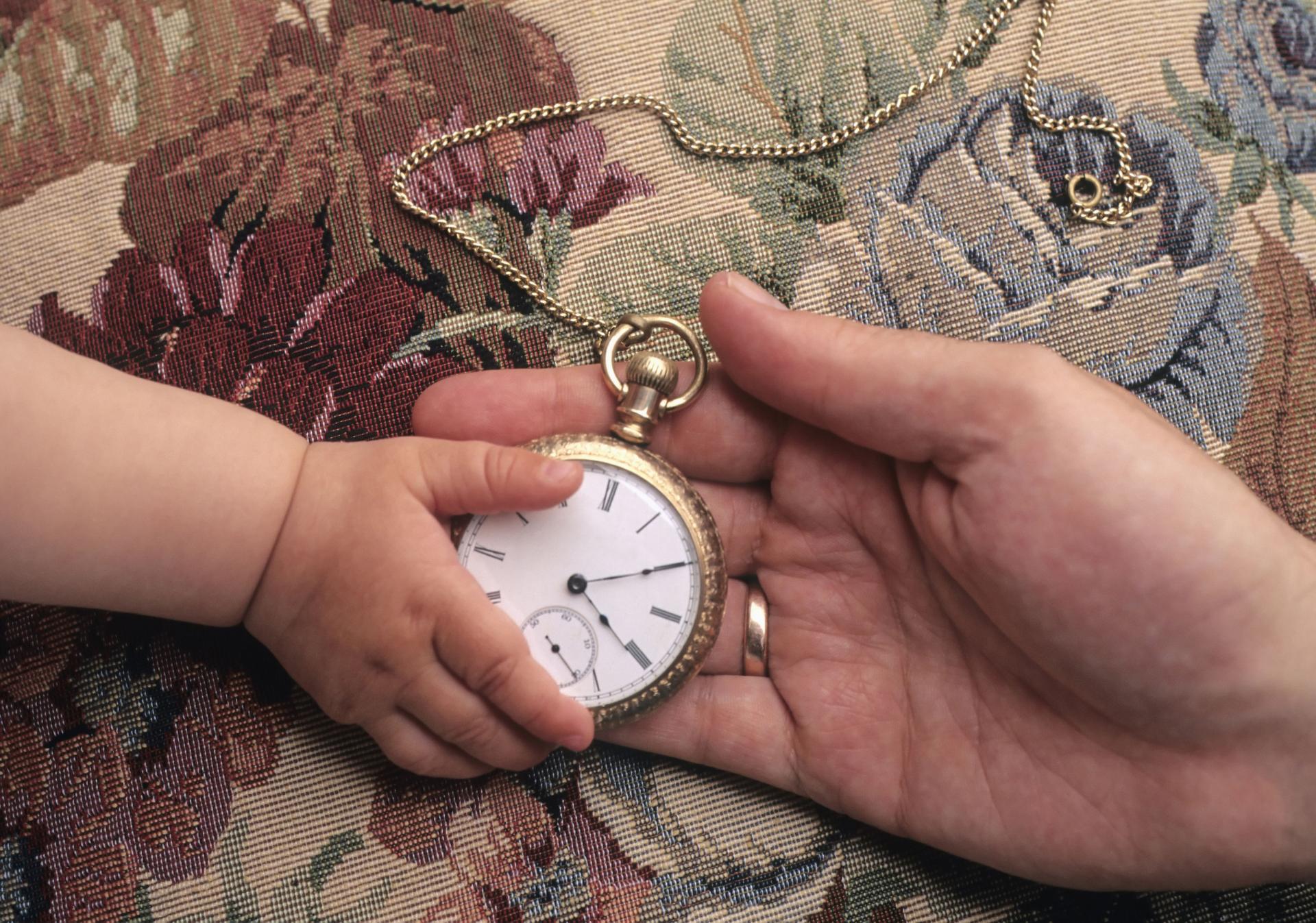 Crédit photo : © Edward J Bock 111 | Dreamstime.com Main d'un enfant tenant une montre à gousset dans la paume d'un adulte sur un tissu à motifs floraux.